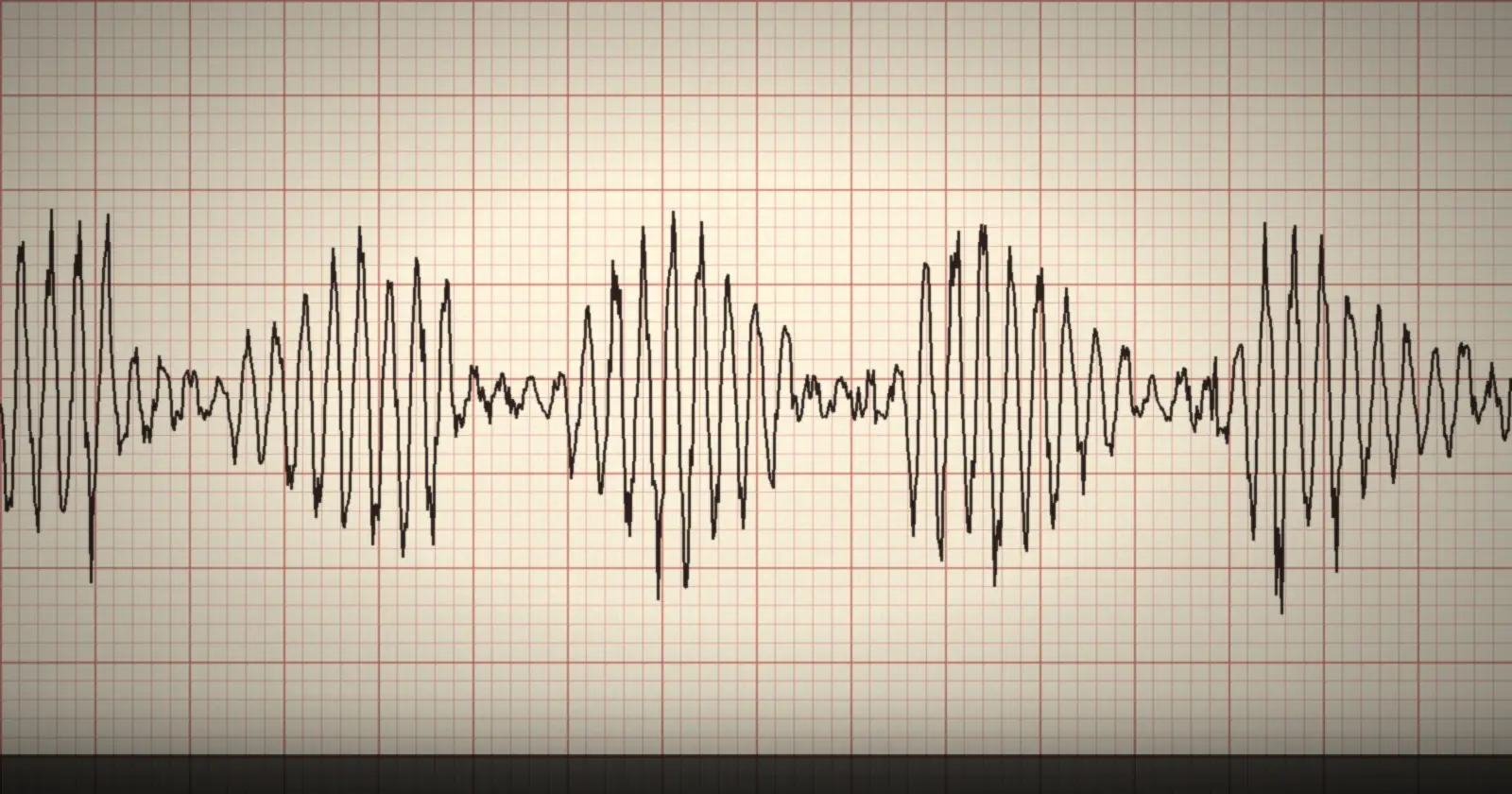 A strip of heated chart paper with a jagged black voice-stress trace drawn across a red grid